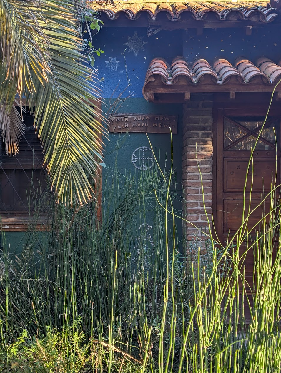 Cartel de madera en una fachada de Ciudad Jardín. Lectura probable: “TAIN RUKA MEW / TAIN MAPU MEW”. Foto: archivo particular, 2026.