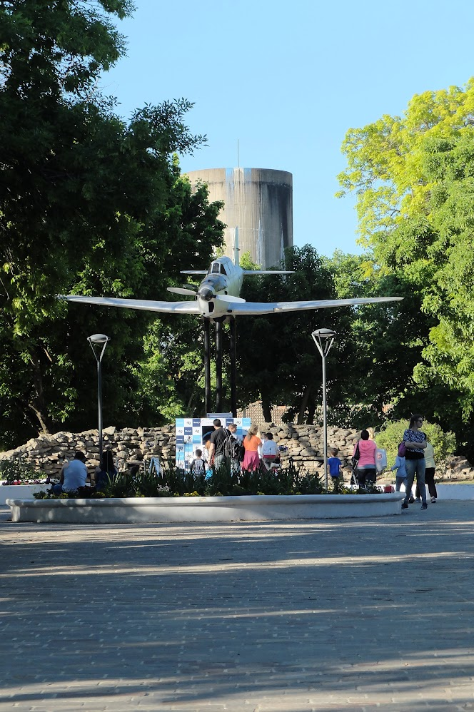 El Fiat G-46B elevado sobre la plaza. Atrás aparece la infraestructura alta del barrio, como telón raro y perfecto.
