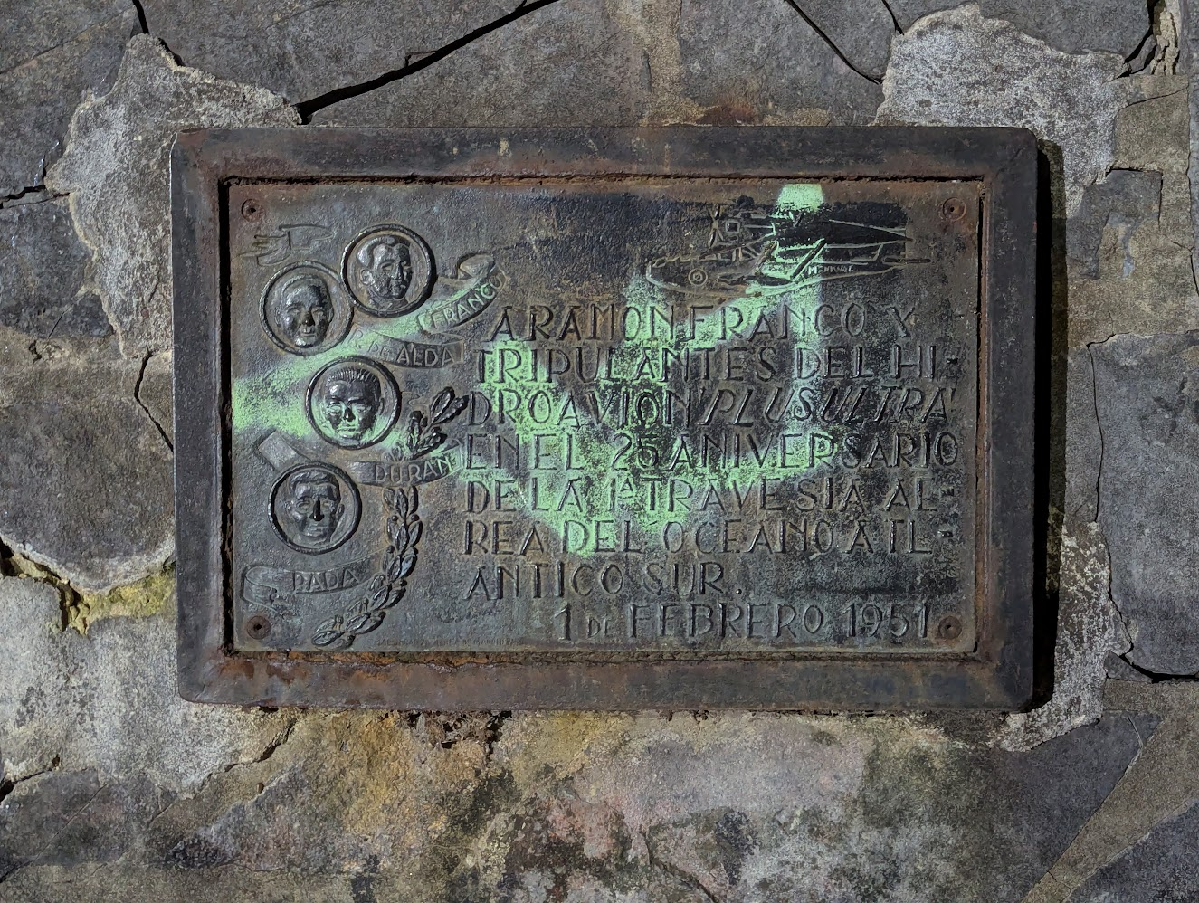 Detalle de la placa. La lectura completa está erosionada, pero se distinguen el homenaje, la fecha y los cuatro nombres de la tripulación.
